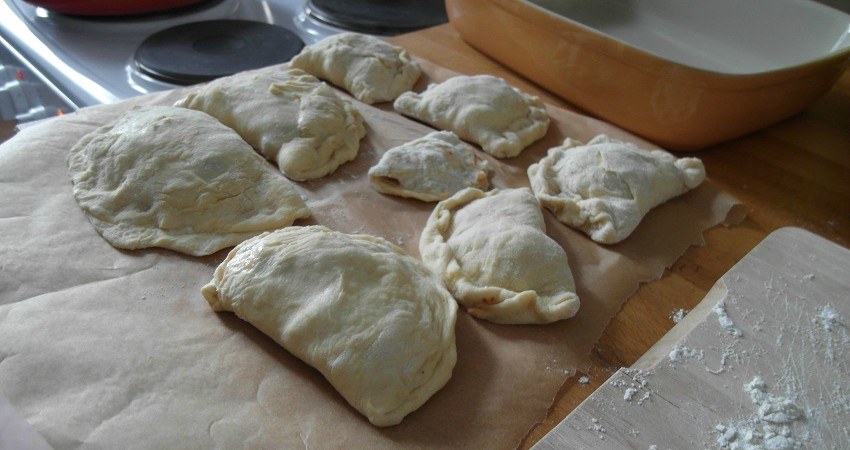 Empanadas Rezept aus Chile: Ein Blech mit rohen Empanadas ist bereit in den Ofen geschoben zu werden.