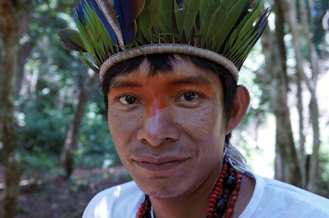Indigene Völker im Amazonasgebiet: Ein Mitglied der Guarani mit einem Haarkranz voller grüner Federn und rot bemalten Augen schaut in die Kamera.