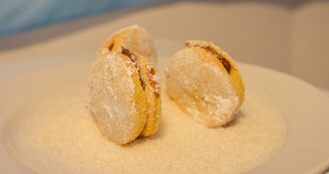 Die klassische Variante der Alfajores aus Argentinien in der Zubereitung: Ein Doppelkeks gefüllt mit Dulce de Leche, bestäubt mit Puderzucker und einem Rand aus Kokosraspeln.